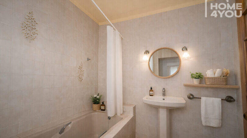 Bright bathroom with bathtub, round mirror, sink and subtle decoration in the multi-family house Felanitx