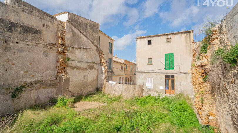 Dilapidated property in Felanitx with old stone walls, overgrown vegetation and view of neighboring buildings