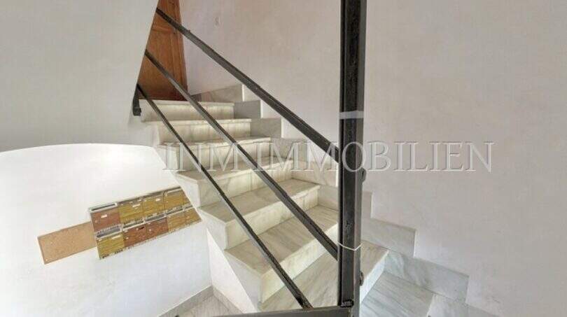 Luminosa escalera con escalones de mármol y barandilla de hierro forjado en apartamento renovado en Palma de Mallorca.