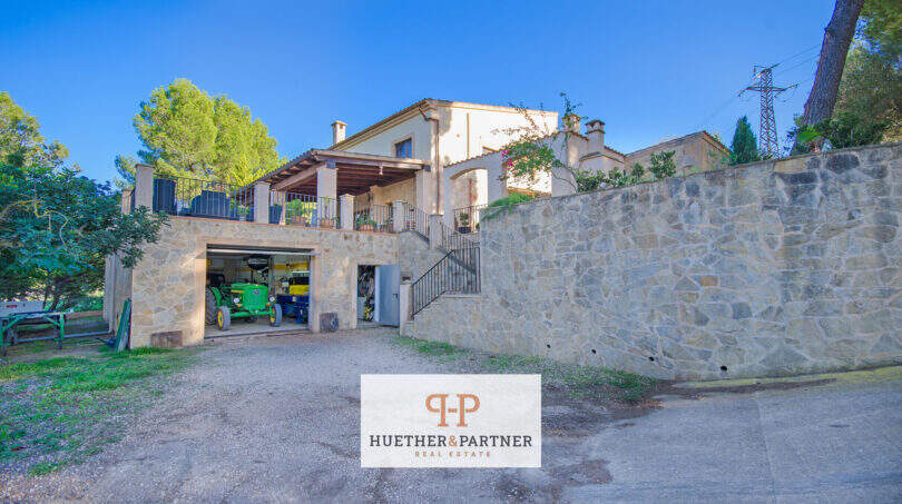 Außenansicht Finca Son Macià mit Natursteinmauer, Garage mit Traktor und überdachter Terrasse im Obergeschoss.