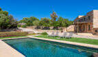 Finca Esporles: Großer Pool mit Liegestühlen, Natursteinhaus und mediterranem Garten unter blauem Himmel.