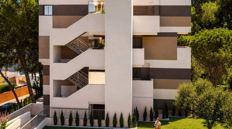 Modernes Penthouse-Gebäude in Canyamel mit Außenpool, Grünfläche und Balkonen, umgeben von Pinien.