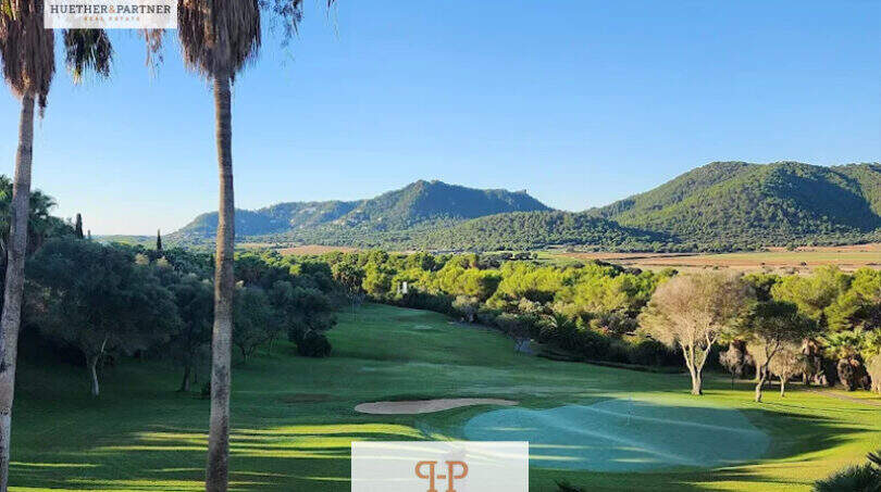 Penthouse Canyamel: Panoramablick auf Golfplatz, Pinienwald und Berge unter strahlend blauem Himmel.