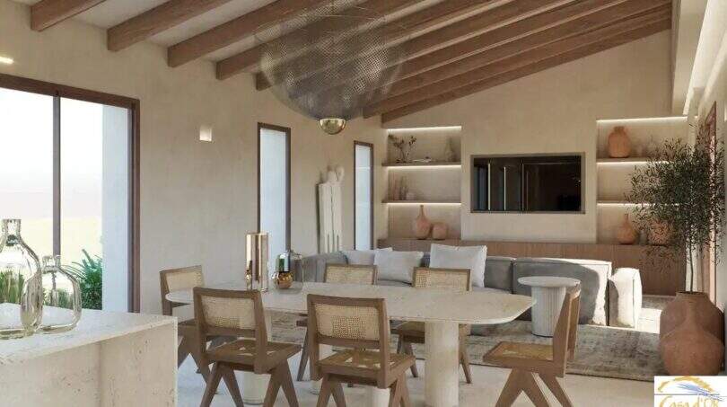 Salón-comedor diáfano de la Finca Artà, con techo de vigas de madera, sillas de ratán y un ambiente mediterráneo.