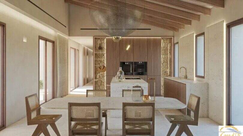 Salón-comedor diáfano con techo de vigas de madera, suelos de imitación de mármol y una cocina moderna en esta exclusiva finca de Artà