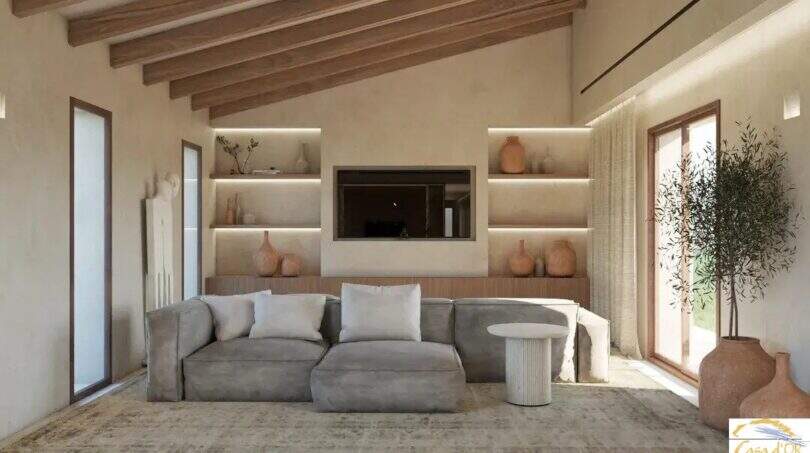 Luminoso salón de la Finca Artà con techo de vigas de madera, estantería empotrada, sofá gris y enlucido de piedra natural de estilo mediterráneo.