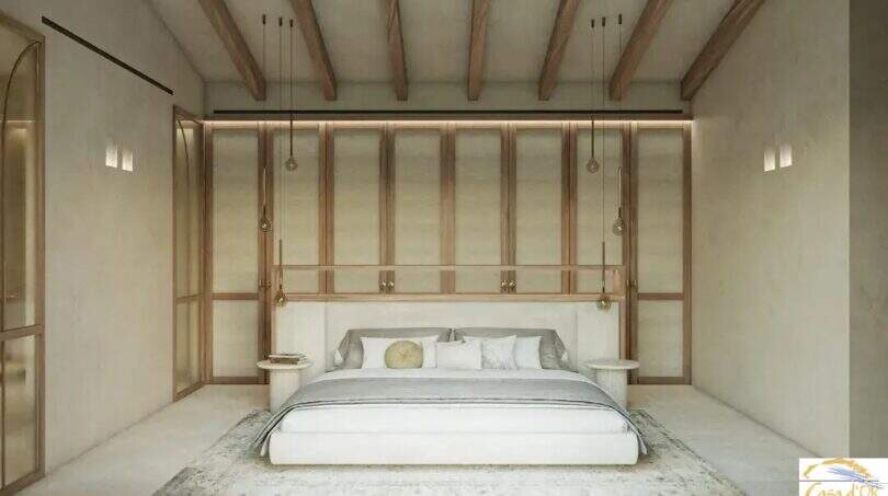Luminoso dormitorio de la finca de Artà, con techo de vigas de madera, una elegante cama de matrimonio y modernas lámparas colgantes.