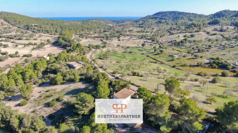 Luftaufnahme einer Finca in Son Macià, umgeben von Wäldern und Feldern, mit Meerblick im Hintergrund.