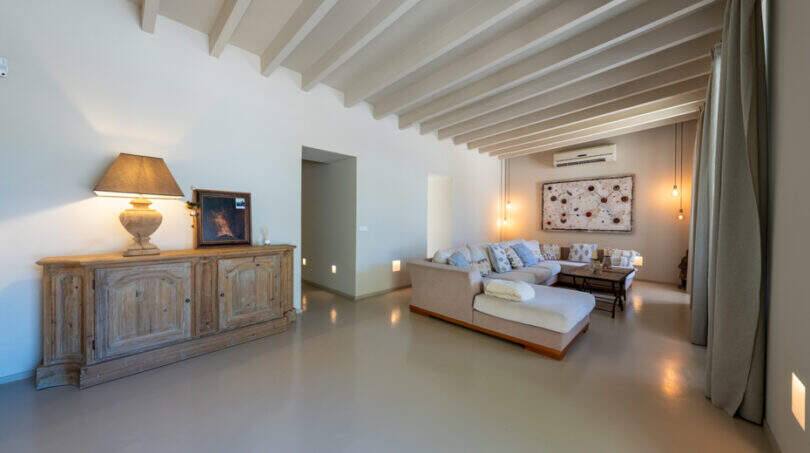 Helles Wohnzimmer der Finca in Esporles mit Holzbalkendecke, elegantem Sofa und rustikalem Sideboard.