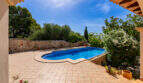 Terraza soleada con piscina, suelo de baldosas, muro de piedra natural y jardín mediterráneo de la villa familiar en Cala Murada