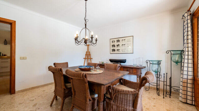 Comedor rústico de la villa de Cala Murada, con mesa de madera, sillas de mimbre y una elegante lámpara de araña.