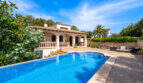 Villa mediterránea en Cala Murada con una gran piscina rectangular, terraza y una exuberante vegetación bajo un cielo azul.