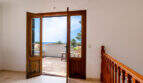 Pasillo luminoso con escalera de madera y puerta abierta a la terraza con vistas al mar, Villa Cala Murada