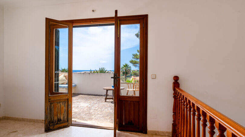 Pasillo luminoso con escalera de madera y puerta abierta a la terraza con vistas al mar, Villa Cala Murada