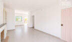 Heller Wohnbereich mit Kamin, rosa Eingangstür, Terrakottafliesen und Fenster mit Gartenblick in Cala Llombards
