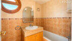 Badezimmer mit Badewanne, Holzwaschtisch, rundem Bullauge-Fenster und beigen Fliesen in Wohnung Llucmajor