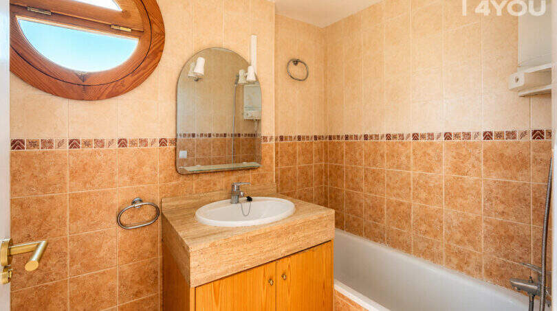 Badezimmer mit Badewanne, Holzwaschtisch, rundem Bullauge-Fenster und beigen Fliesen in Wohnung Llucmajor