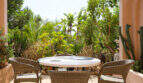 Überdachte Terrasse mit Rattanmöbeln und Marmorrundetisch, umgeben von üppiger mediterraner Gartenvegetation beim Agroturismo Ses Salines