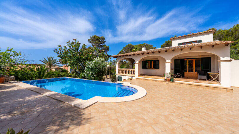Villa de estilo mediterráneo en Cala Murada con una gran piscina, terraza y arcadas bajo el cielo azul.