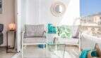 Balcón soleado del apartamento en primera línea de mar en Port Adriano con muebles lounge, mesa de cristal y vistas al mar