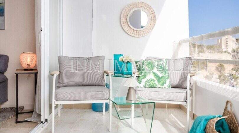 Balcón soleado del apartamento en primera línea de mar en Port Adriano con muebles lounge, mesa de cristal y vistas al mar