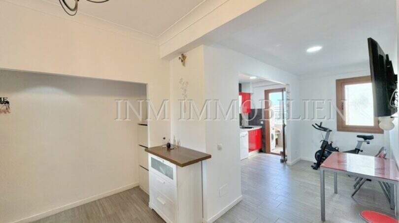 Luminosa zona de estar con suelo de madera, cocina abierta en rojo y área de fitness en apartamento renovado en Palma