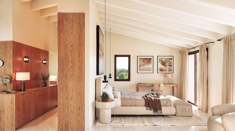 Helles Schlafzimmer der Luxusfinca Ses Salines mit Holzelementen, Dachschräge und elegantem Bett