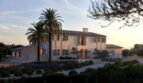 Außenansicht einer modernen Luxusfinca in Ses Salines mit Palme, mediterranem Garten und elegantem Eingangsbereich bei Abenddämmerung.