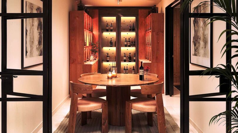 Elegantes Weinzimmer mit beleuchtetem Holzregal, rundem Esstisch und vier Stühlen in Luxusfinca Ses Salines.