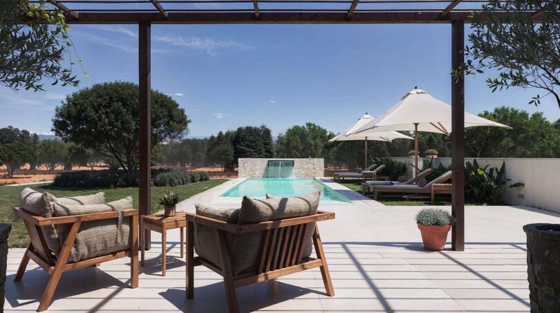 Luxusfinca Ses Salines: Überdachte Terrasse mit Holzmöbeln, Pool mit Wasserfall und Sonnenschirmen im Grünen.