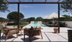 Luxusfinca Ses Salines: Elegante Pergola-Terrasse mit Holzmöbeln, Pool mit Wasserfall und Sonnenliegen im Freien.
