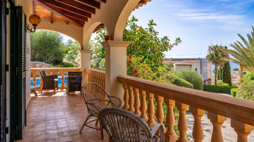 Terraza cubierta de la villa de Cala Murada, con arcos, sillas de ratán y vistas a la piscina y al jardín.