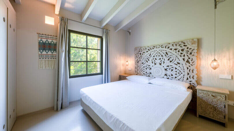 Helles Schlafzimmer mit ornamentalem Holzkopfteil, weißer Bettwäsche und Holzbalkendecke in Finca Esporles