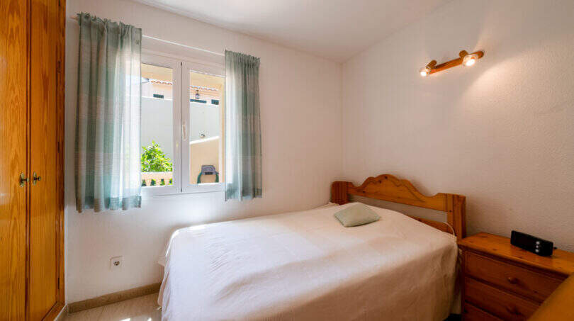 Helles Schlafzimmer mit Einzelbett, Kiefernholzmöbeln und mintgrünen Vorhängen im Doppelhaus Cala Murada.