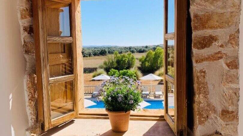 Rustikales Steinmauerwerk-Fenster mit Holzrahmen, Blumentopf und Blick auf Pool und Landschaft des Agroturismo