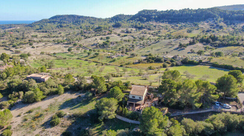 Luftaufnahme einer Finca in Son Macià, umgeben von grüner Landschaft, Feldern und Hügeln mit Meerblick.