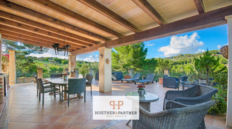 Überdachte Terrasse der Finca Son Macià mit Holzbalkendecke, Lounge-Möbeln und Panoramablick ins Grüne.