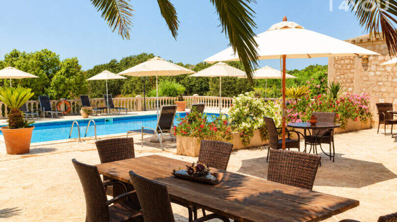 Sonnige Poolterrasse mit Rattanmöbeln, Sonnenschirmen und Blumen eines Agroturismos bei Ses Salines