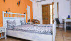 Helles Schlafzimmer mit weißem Holzbett, orangefarbener Akzentwand und Terrakottaboden im Agroturismo Ses Salines