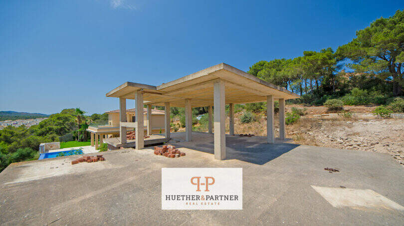Rohbau mit Betonstützen und Flachdach in Cala Romántica, im Hintergrund fertige Villa mit Pool und Meerblick