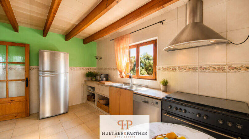 Rustikale Küche der Finca Felanitx mit Holzbalkendecke, Edelstahlkühlschrank, schwarzem Herd und grüner Akzentwand