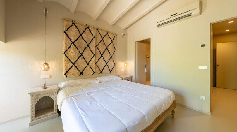 Helles Schlafzimmer der Finca mit Doppelbett, Klimaanlage und Berberteppich als Wanddekoration.