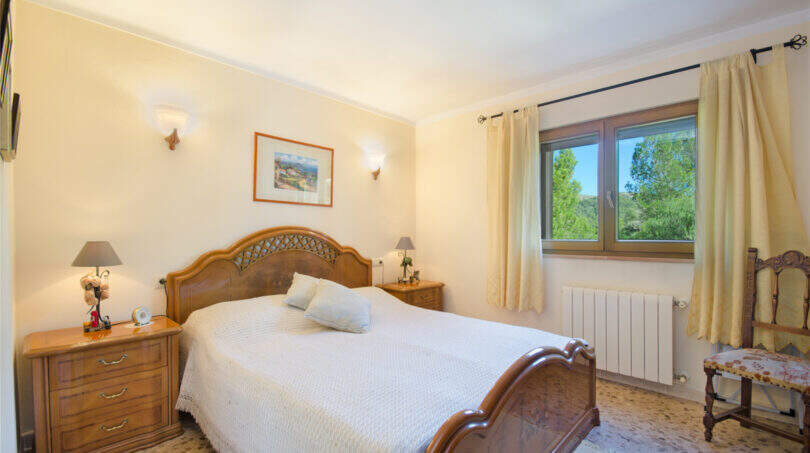 Helles Schlafzimmer der Finca Son Macià mit elegantem Holzbett, Nachttischen und Fenster mit Gartenblick.