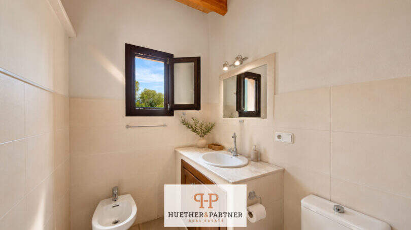 Helles Badezimmer der Finca Felanitx mit Bidet, Waschtisch, Spiegel und Holzbalkendecke