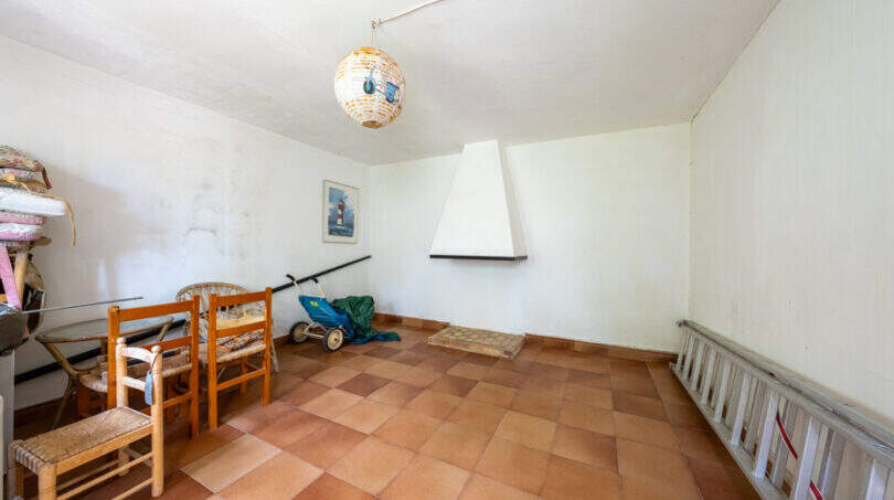 Habitación sin utilizar con suelo de terracota, chimenea y sillas de madera en la villa familiar Cala Murada
