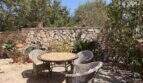 Mediterraner Innenhof mit Rattanmöbeln, Mosaiktisch und historischer Natursteinmauer, umgeben von üppiger Bepflanzung.