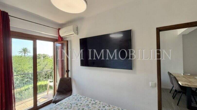 Luminoso dormitorio con cama doble, televisor montado en pared, aire acondicionado y balcón con vista al verde en Palma.