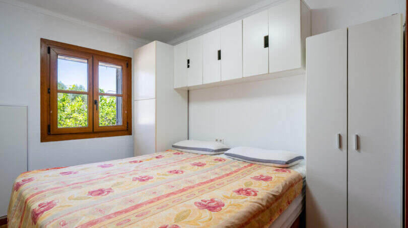 Schlafzimmer mit Doppelbett, Blumendecke, weißen Einbauschränken und Holzfenster mit Gartenblick in Cala Murada