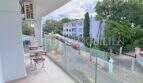 Moderner Balkon mit Glasgeländer und Gartenmöbeln, Blick auf Straße und weiße Gebäude in Palmanova