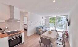 Open-concept living-dining area with a modern kitchen, dining table, and sofa, and a large window wall in the Palmanova apartment